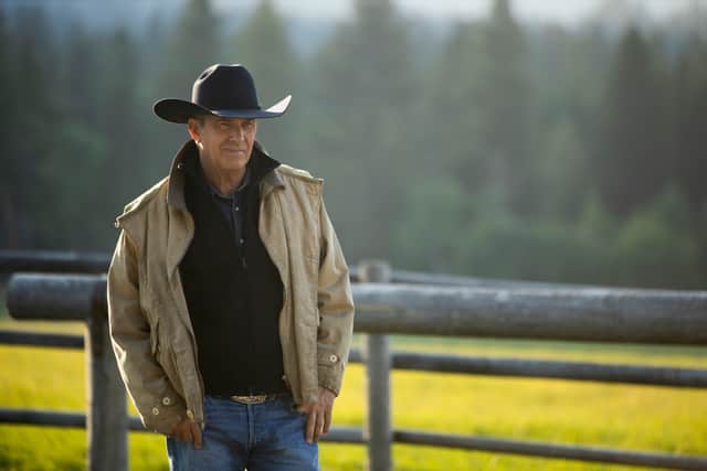 Kevin Costner as John Dutton in Yellowstone, stood in a field next to a fence, his hands in his pockets, wearing a cowboy hat (Credit: Paramount+)