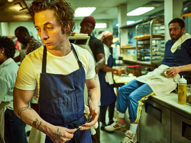 Jeremy Allen White as Carmen ‘Carmy’ Berzatto in The Bear, wearing a blue apron, holdin a spoon in a restaurant kitchen (Credit: Frank Ockenfels/FX )