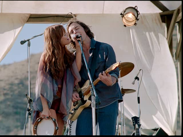 Riley Keough as Daisy Jones and Sam Claflin as Billy Dunne in Daisy Jones & The Six, singing into a shared microphone (Credit: Lacey Terrell/Prime Video)