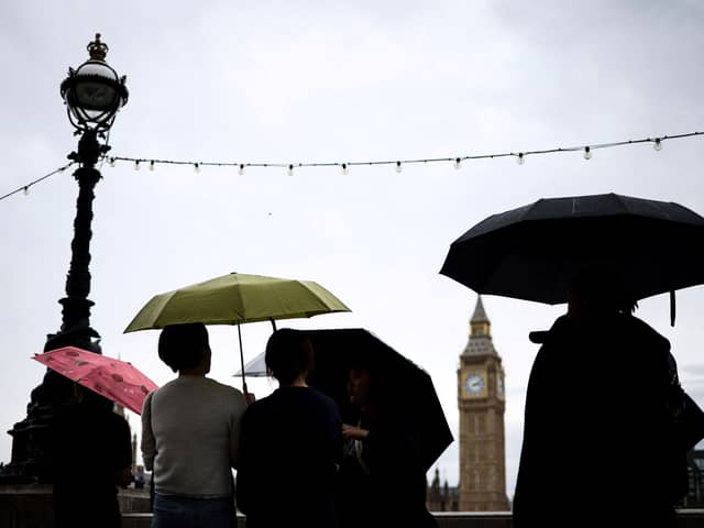 Pedestrian stand under umbrellas while looking at Elizabeth Tower, commonly called Big Ben from the Southbank by the River Thames, in central London, on July 31, 2023 on a gloomy and rainy summer day.