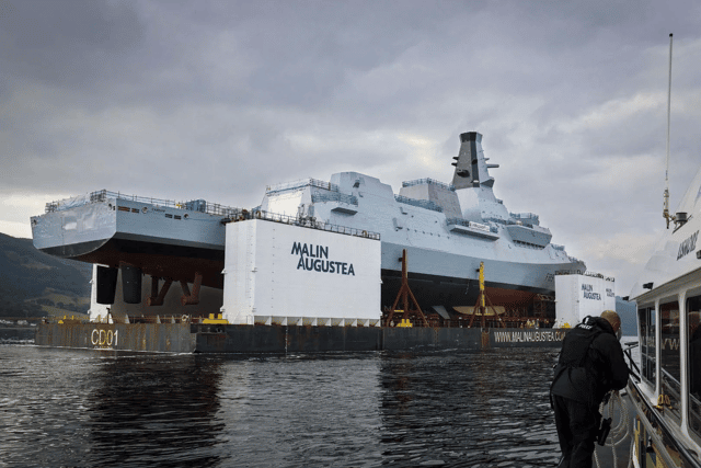 HMS Cardiff being transported on a barge along the River Clyde, before slowly being lowered into the water.