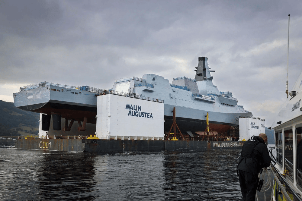 HMS Cardiff being transported on a barge along the River Clyde, before slowly being lowered into the water.