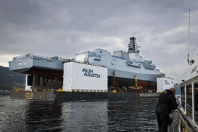HMS Cardiff being transported on a barge along the River Clyde, before slowly being lowered into the water.