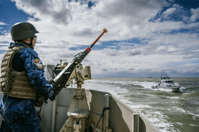 A Belgian sailor with a heavy machine-gun watches as HMS Exploit charges past his minehunter. HMS Exploit and HMS Blazer, two Portsmouth ships, have been seen "causing havoc" in the North Sea and disrupting European ships.