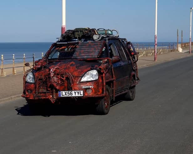 A zombie themed vehicle driving on a road by the coast
