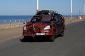 A zombie themed vehicle driving on a road by the coast