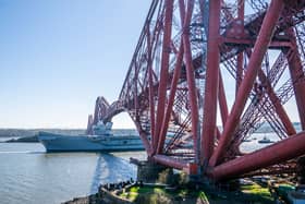 HMS Queen Elizabeth passes under the Forth Bridge heading out to sea after leaving Rosyth, The Royal Navy aircraft carrier is back on the water after months on the side-lines.