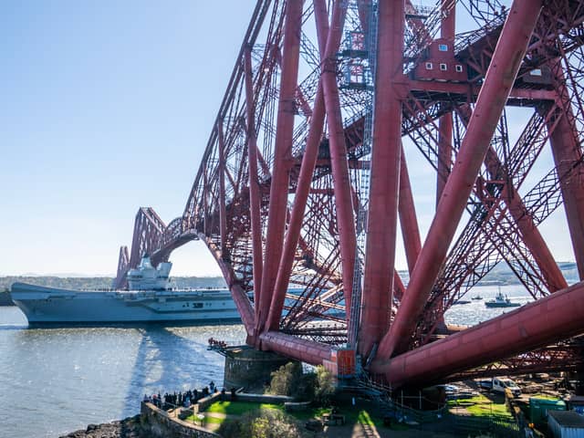 HMS Queen Elizabeth passes under the Forth Bridge heading out to sea after leaving Rosyth, The Royal Navy aircraft carrier is back on the water after months on the side-lines.