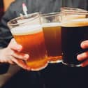 Friends cheering with beer glasses sitting around cafe bar table - Group of multiracial people toasting and clinking drinks at each others health inside pub - Vintage nostalgic old times filter look