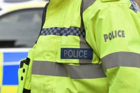 A police officer wearing a hi-vis jacket beside police car