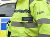 A police officer wearing a hi-vis jacket beside police car
