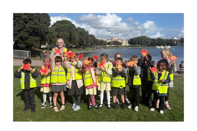 Pupils from Bramble Infant School and Nursery with their Year 2 teacher Fiona Shellard, proudly holding up their paper crabs by Canoe Lake, Southsea. Credit: University of Portsmouth. 