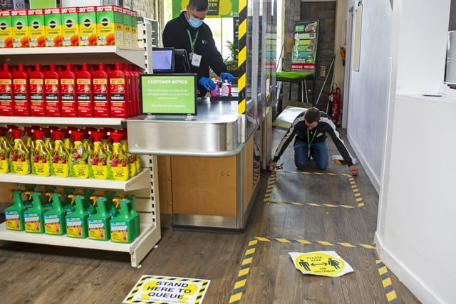 Measures include 'Stand Here to Queue' signs and hashed tape across the store