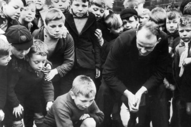 A crowd of pupils of Whitwood Mere School in Castleford, Yorkshire, watching a fellow pupil competing in a game of marbles. The winner will represent the school in an inter-school match on Shrove Tuesday.