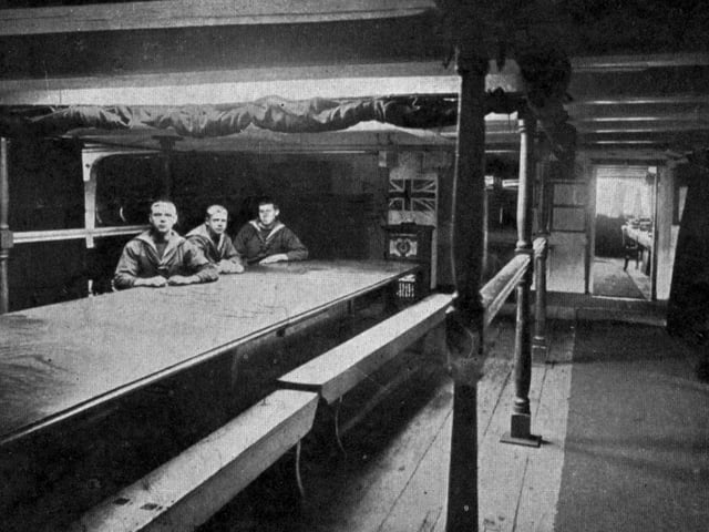 Nelson's cabin on HMS Victory circa 1910.Taken in Horatio Nelson's cabin on board HMS Victory. At this time of course the Victory was still moored  in Portsmouth Harbour, where tourists used to pay a ferryman to get out to her. As the sailors are wearing sea jerseys under their jackets, it must be wintertime.
