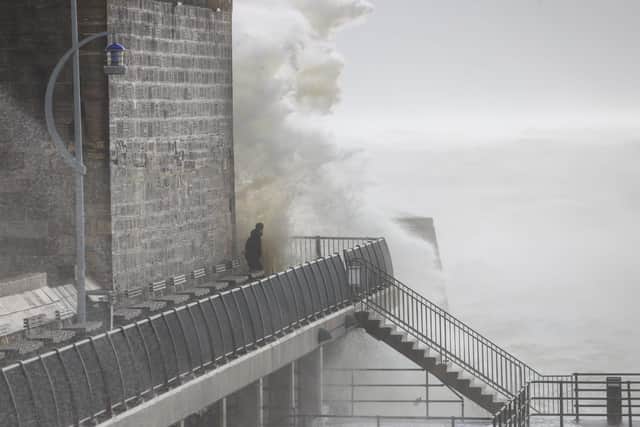 A huge wave slams into the Hotwalls in Old Portsmouth, drenching a bystander on the harbour pathway. Photo: Alex Shute