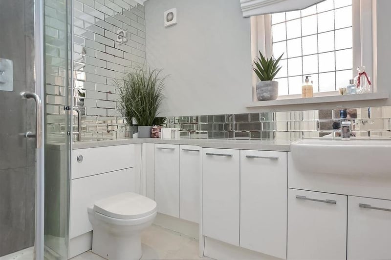 The attractive family-bathroom features a modern four-piece suite with chrome fittings. It comprises a bathtub, corner shower cubicle with sliding, glazed doors and large vanity unit with inset wash hand basin, plus a substantial range of storage cupboards.