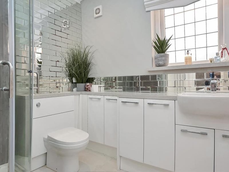 The attractive family-bathroom features a modern four-piece suite with chrome fittings. It comprises a bathtub, corner shower cubicle with sliding, glazed doors and large vanity unit with inset wash hand basin, plus a substantial range of storage cupboards.