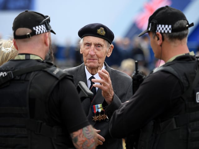Former British Royal Marine, and D-Day veteran Jim Booth (C), talk with armed members of Britain's police.