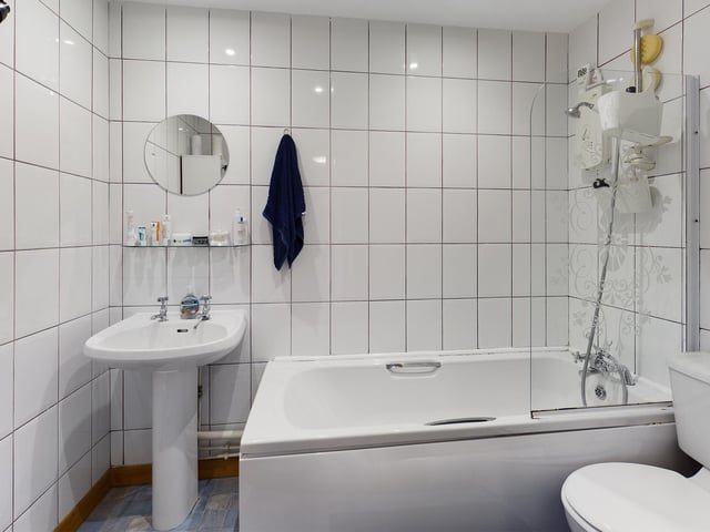 The bathroom is fully tiled with a white suite, a shower over bath and benefits from a towel rail.