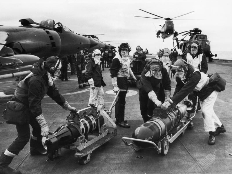 Armourers moving torpedoes on the flight deck of HMS Hermes during the Falklands conflict, May 1982. The torpedoes are to re-arm Sea King helicopters to counter the threat from Argentinian submarines.