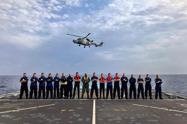 A Wildcat helicopter flies above some of the flight crew on HMS Trent in the Mediterranean