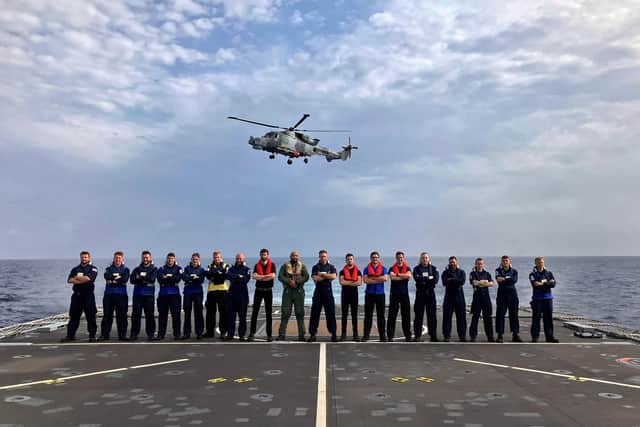 A Wildcat helicopter flies above some of the flight crew on HMS Trent in the Mediterranean