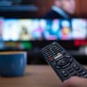 Netflix remote control with TV behind in evening with Netflix menu (Shutterstock)