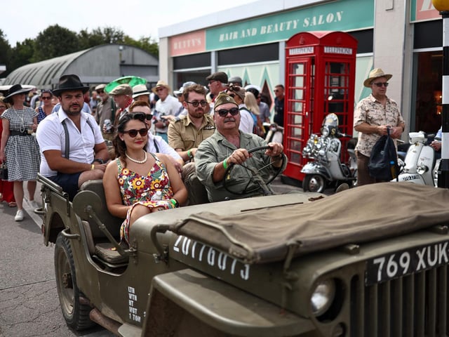 People wearing period clothing drive a classic car during the opening day of Goodwood Revival at the Goodwood Motor Circuit in Chichester on September 8, 2023. The only historic motor race meeting to be staged entirely in a period theme, Goodwood Revival is an immersive celebration of iconic cars and fashion.