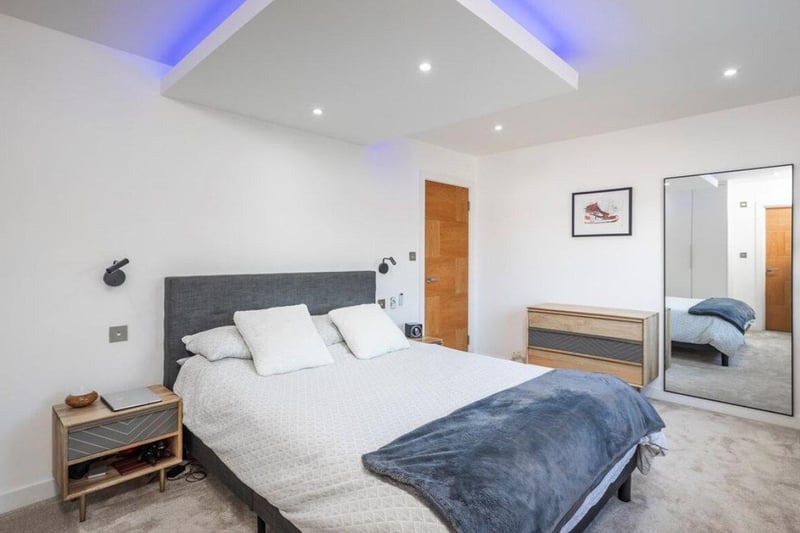The listing says: "The reception hallway has a beautiful floating staircase with glass panels and mood lighting set against a feature flint wall."