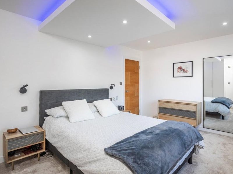 The listing says: "The reception hallway has a beautiful floating staircase with glass panels and mood lighting set against a feature flint wall."