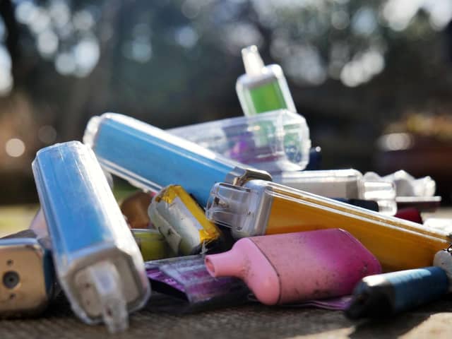 Discarded electronic cigarette vapes that have been collected from roads and pavements shot over a pale concrete slab background