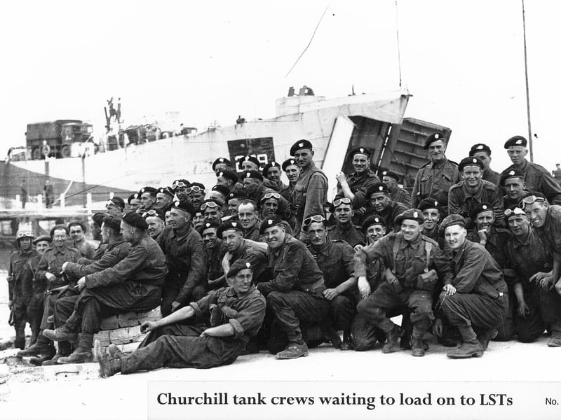 Crewmen from British Churchill tanks, waiting at (probably) Stokes Bay to load onto the LST behind. On the left are several of the concrete blocks that the embarkation 'hards' were made from: several men are sitting on some.