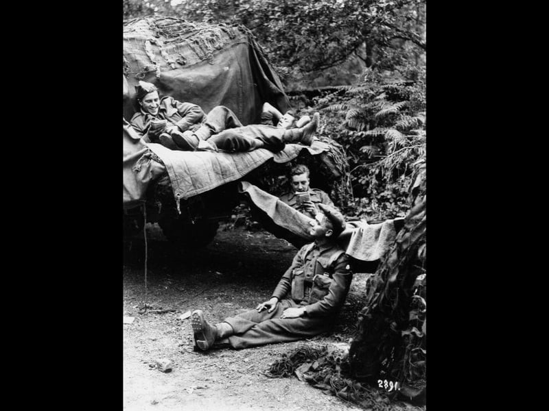 Four soldiers waiting next to a vehicle shortly before [or possibly just after] D-Day, somewhere not far from Portsmouth. Probably at one of the troop camps out in the countryside north of the city, or at a roadside near one of those camps that was designated for waiting troops.