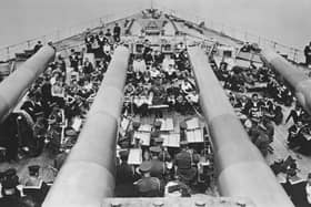 Seen from the view of the BL 14-inch (360 mm) Mark VII guns of the forward A turret of HMS Prince of Wales, a King George V-class battleship, a British Army military band performs a concert for the Royal Navy crew on 4th December 1941 at anchor in Sembawang naval dockyard, Singapore. On 10th December 1941 in the South China Sea off Malaya (present-day Malaysia), HMS Prince of Wales and the battlecruiser HMS Repulse were sunk by land-based bombers and torpedo bombers of the Imperial Japanese Navy. 840 sailors from both ships were lost in the engagement including Captain John Leach, Captain of HMS Prince of Wales.  (Photo by Central Press/Hulton Archive/Getty Images)