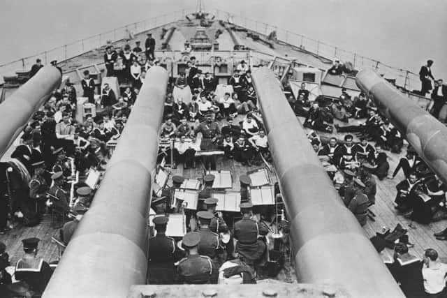 Seen from the view of the BL 14-inch (360 mm) Mark VII guns of the forward A turret of HMS Prince of Wales, a King George V-class battleship, a British Army military band performs a concert for the Royal Navy crew on 4th December 1941 at anchor in Sembawang naval dockyard, Singapore. On 10th December 1941 in the South China Sea off Malaya (present-day Malaysia), HMS Prince of Wales and the battlecruiser HMS Repulse were sunk by land-based bombers and torpedo bombers of the Imperial Japanese Navy. 840 sailors from both ships were lost in the engagement including Captain John Leach, Captain of HMS Prince of Wales.  (Photo by Central Press/Hulton Archive/Getty Images)