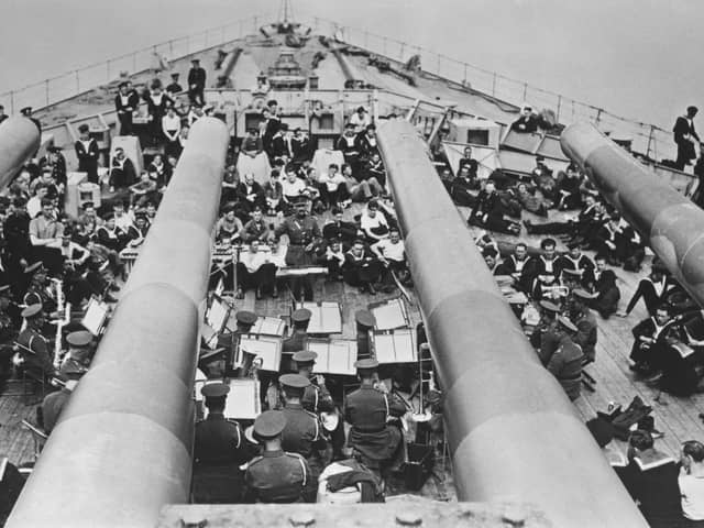 Seen from the view of the BL 14-inch (360 mm) Mark VII guns of the forward A turret of HMS Prince of Wales, a King George V-class battleship, a British Army military band performs a concert for the Royal Navy crew on 4th December 1941 at anchor in Sembawang naval dockyard, Singapore. On 10th December 1941 in the South China Sea off Malaya (present-day Malaysia), HMS Prince of Wales and the battlecruiser HMS Repulse were sunk by land-based bombers and torpedo bombers of the Imperial Japanese Navy. 840 sailors from both ships were lost in the engagement including Captain John Leach, Captain of HMS Prince of Wales.  (Photo by Central Press/Hulton Archive/Getty Images)