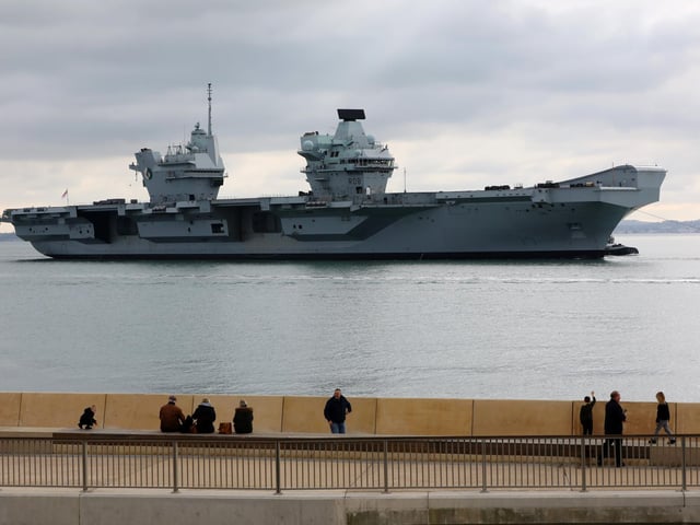 HMS Queen Elizabeth passes the newly reopened walkway on the sea defences at Long Curtain Moat, as she returns to Portsmouth Naval Base