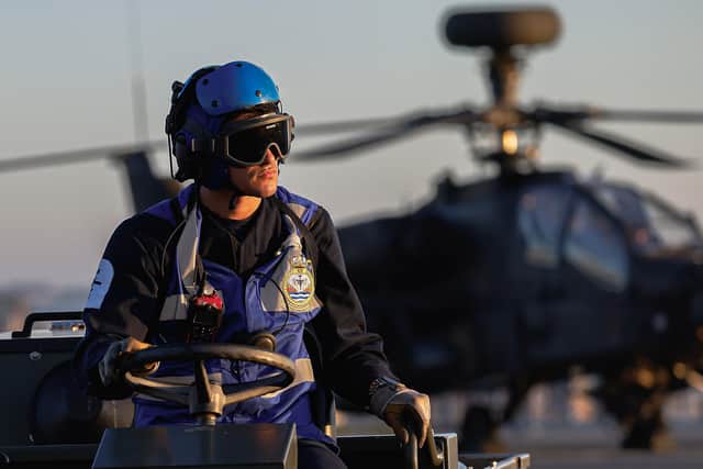 One of HMS Prince of Wales's ship's company pictured on the ship's flight deck with an Apache helicopter in the background.