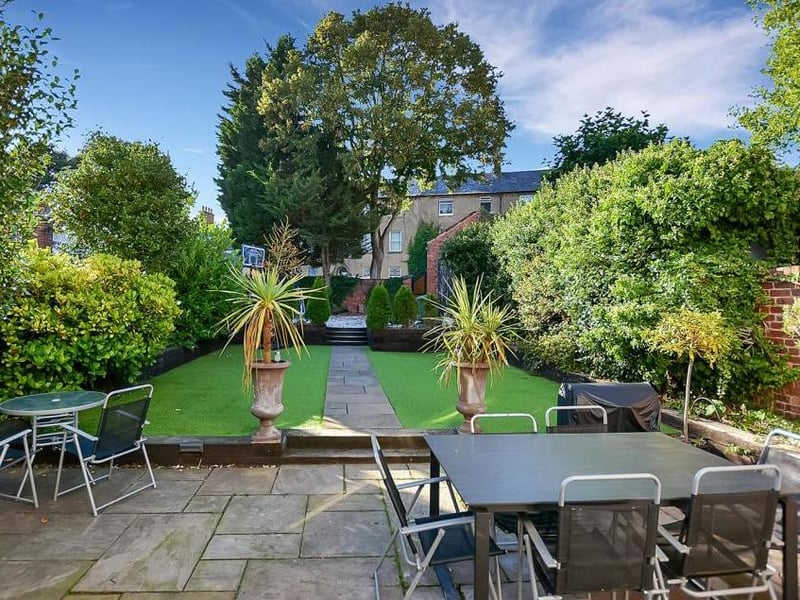 The back garden features this large Indian sandstone patio area. It is surrounded by 'railway sleepers' offering brick inset lighting, while steps lead to an artificial lawn.