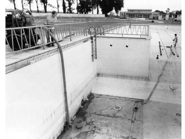 Pool supervisor Mr Padmore (left) and pool assistant N. Goddard pump out remnants of the winter's rain ready for refilling in 1981.