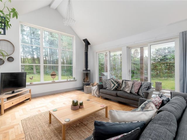 The family room is open plan to the kitchen/dining room and has a contemporary log burner, double height vaulted ceiling, full height windows, and sliding doors leading out onto the barbecue area.