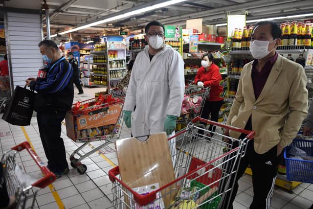 A worker wears protective clothing as a preventive measure against the Covid-19 coronavirus as he watches over customers to ensure they queue a meter apart in a supermarket in Beijing on March 30. (Photo by GREG BAKER/AFP via Getty Images)