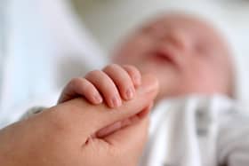 A new born baby grasps the thumb of her mother
