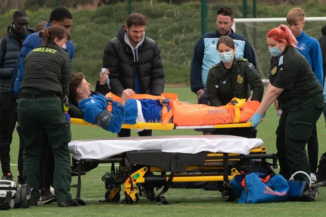 Clanfield captain Will Martin is treated by ambulance staff after breaking his leg, leading to the abandonment of his club's cup tie with Denmead at Front Lawn. Picture: Keith Woodland