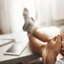 Cup of tea and chill. Woman lying on couch, holding legs on coffee table, drinking hot coffee and enjoying morning, being in dreamy and relaxed mood. Girl in oversized shirt takes break at home.