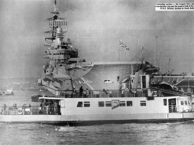 Contrasting carriers. The Gosport ferry makes yet another routine cross-harbour trip, passing the massive bulk of the aircraft carrier HMS Hermes, berthed at South Railway Jetty. The News 6163-1
