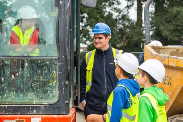 Students trying out the digger for size with Jack Flanagan, Trainee Assistant Site Manager at Bellway South London
