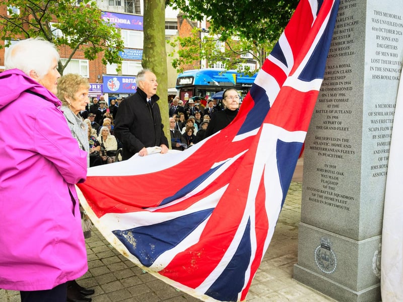 Pictured is: Sons and daughters of the men and boys who were lost in the sinking of HMS Royal Oak, assisted by Sea Cadets from Portsmouth unveil the memorial using the white ensign that was recovered from the wreck of the ship.