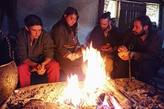 Herigeas Hundas members sat by the fire at Saxon Hall, Butser Ancient Farm, 2021. Picture by Bea Helmes/Herigeas Hundas